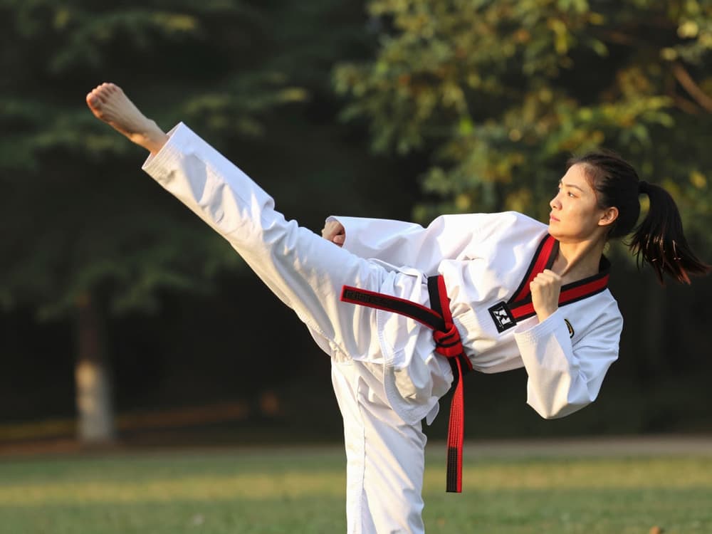 An adult in a red belt throws a side kick in a park at golden hour